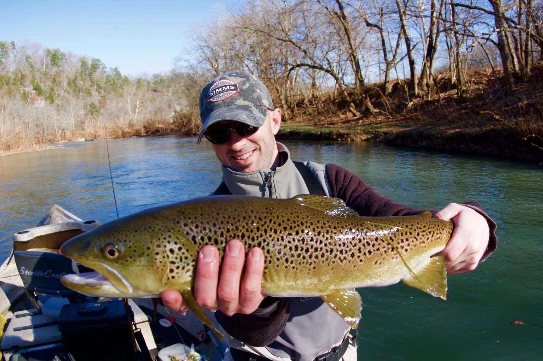 An angler holds a heavily spotted brown trout over the side of a drift boat on a green river